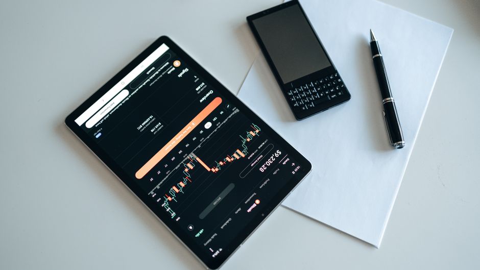 Top view of a workspace with a tablet displaying financial charts, a smartphone, pen